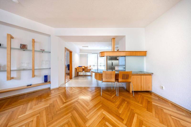 Interior of a 3-room apartment with wood-patterned flooring, a dining area, and an open kitchen.