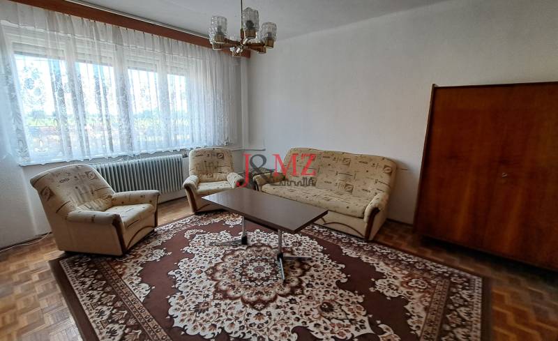 Living room in a family house with a carpet, sofa, and armchairs, large window.