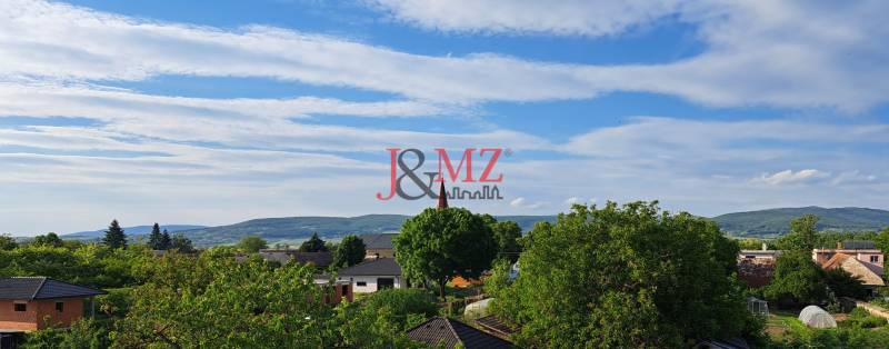 A view of the roofs and greenery of Hronské Kosihy with a view of family houses and mountains.
