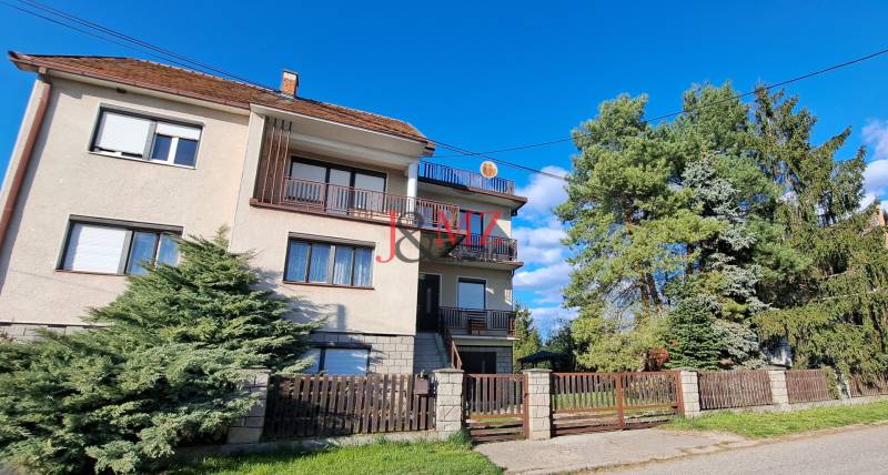 A family house in Hronské Kosihy, with two balconies, a garden, and trees on the property.