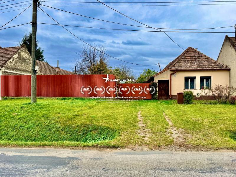 A family house in Budmerice with a red fence and a front garden behind the power lines.