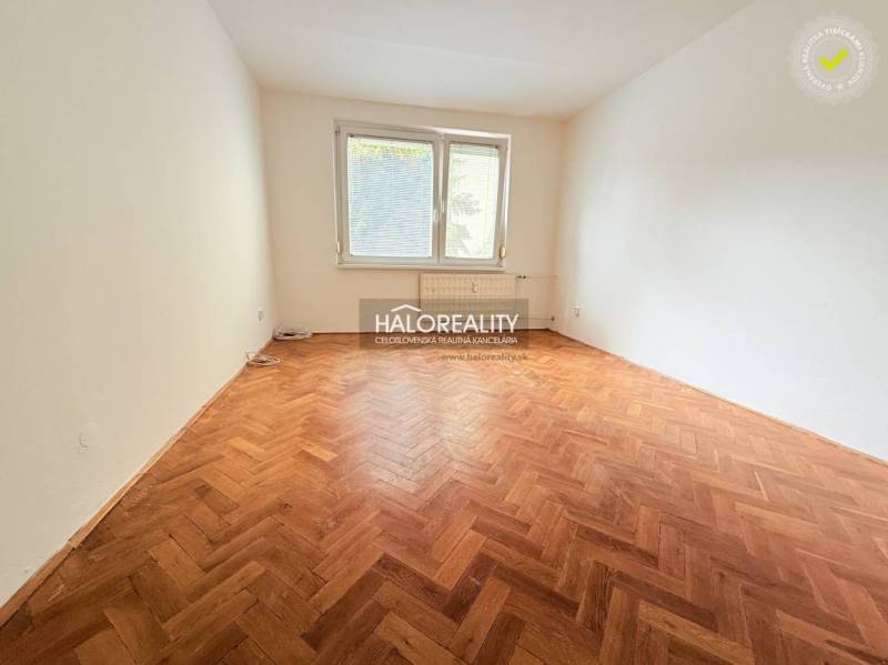 A room in a two-bedroom apartment with a wood-patterned floor and a large window.