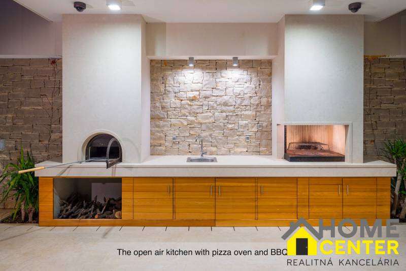 A villa with an outdoor kitchen, stone wall, and pizza oven.