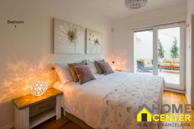 Bedroom in a villa with wood-patterned flooring, delicate paintings, and large windows.