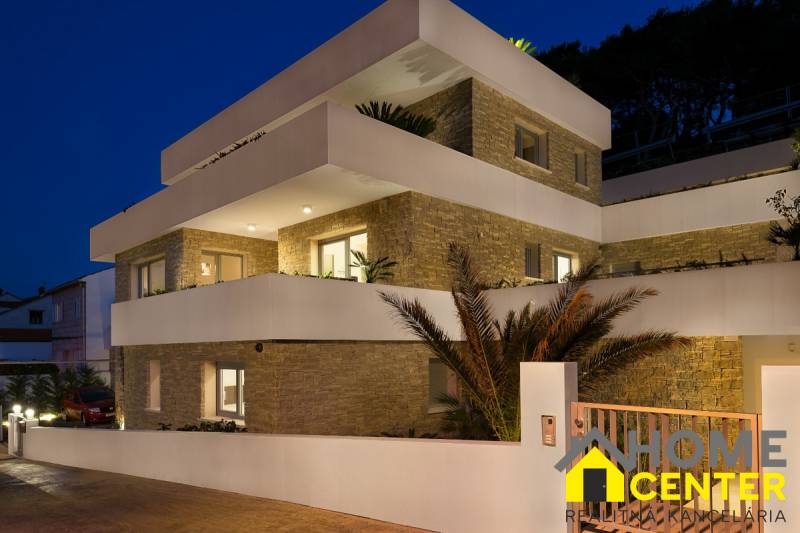 The exterior of a villa in the town of Bol with bright terraces and stone walls at dusk.