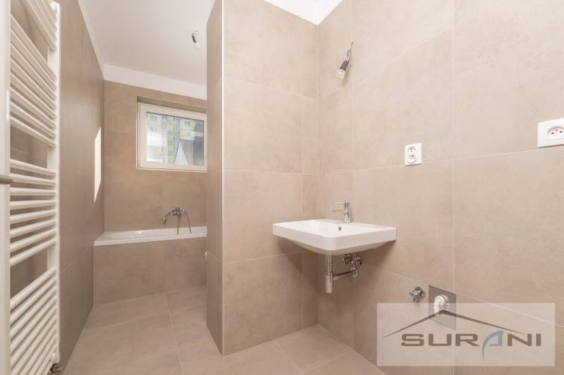 Bathroom in a 2-room apartment with a bathtub, sink, and window. Light tiles.