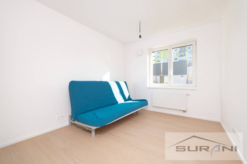 A room in a 2-room apartment with a blue sofa, white walls, and a floor with a wood decor.