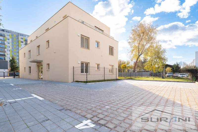 The building on Železničná Street in Bratislava - Vrakuňa, surrounded by a paved area and greenery.