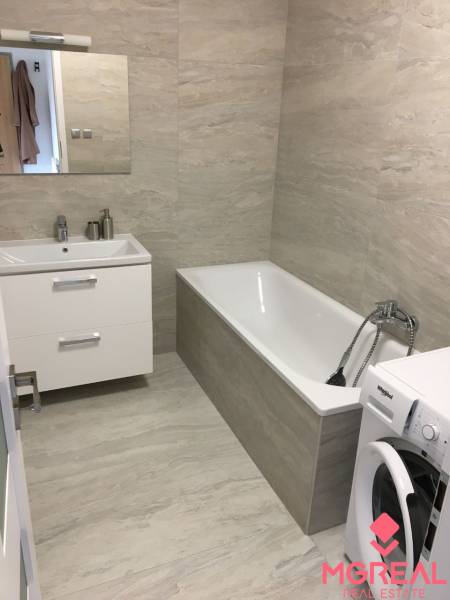 Bathroom with light tiles, bathtub, sink, and washing machine in a studio apartment.