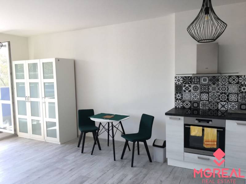 A kitchen in a studio apartment with a wooden decor floor and a dining table.