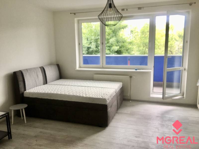 A bright room with a bed, an open balcony, and a floor with a wooden decor.