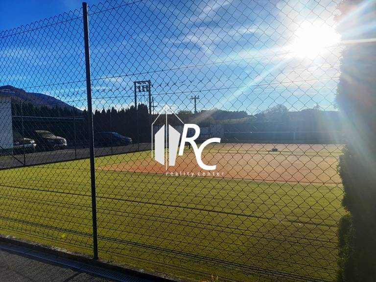 A tennis court by a family house in Necpaly, fenced and illuminated by sunlight.