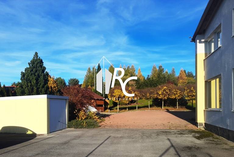 The courtyard of a family house in Necpaly with a paved area and a green background.