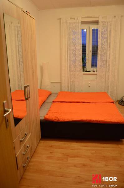 A bedroom in a 2-room apartment with a bed, wardrobe, and wooden decor flooring.