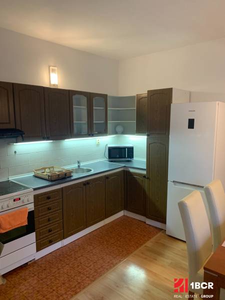 A kitchen with dark cabinets and white appliances in a 2-room apartment, floor with wood decor.