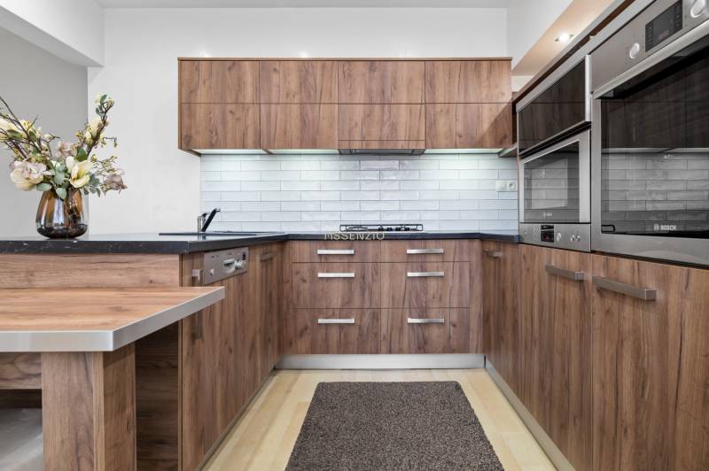 A kitchen in a 2-room apartment with wooden cabinets, white tiles, and a floor with a wooden design.