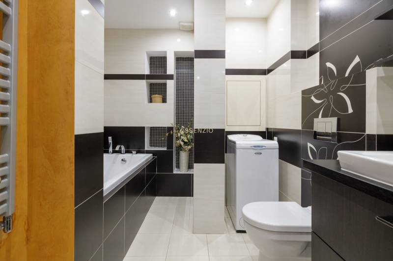 Bathroom in a 2-room apartment with a bathtub, washing machine, toilet, and decorative tiles.