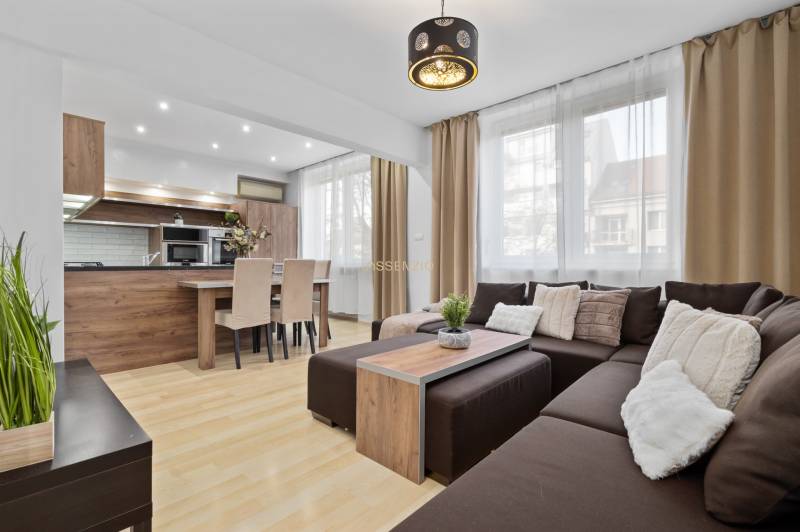 Living room with wood-patterned flooring in a 2-room apartment with a corner sofa and kitchen.