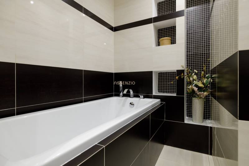 A bathroom with a bathtub and ceramic tiles in a black and white combination in a 2-room apartment.