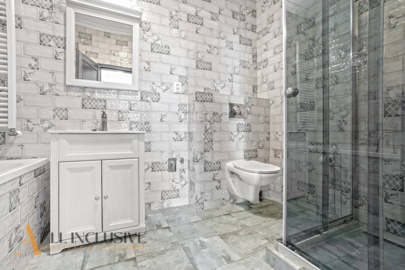 Bathroom in a 2-room apartment with a sink, shower, and decorative tiles.