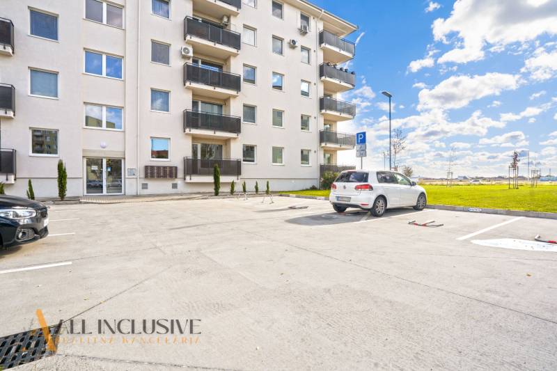 Parking lot in front of the apartment building on Panónsky háj in Dunajská Streda, with cars and a grassy area.