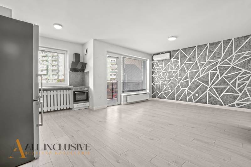 Kitchen and living room in a 2-room apartment with a wooden decor floor and a geometric wall.