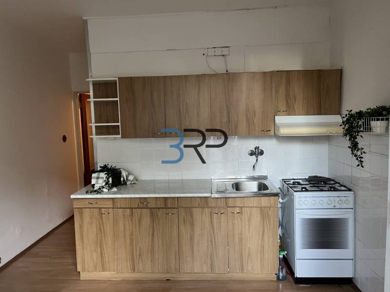 A kitchen in a 2-room apartment with a wood-patterned floor and a gas stove.