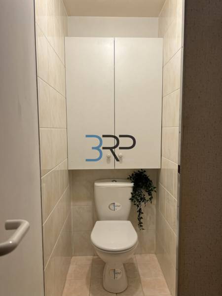 Bathroom with a toilet and a cabinet in a 2-room apartment, neutral tiles.