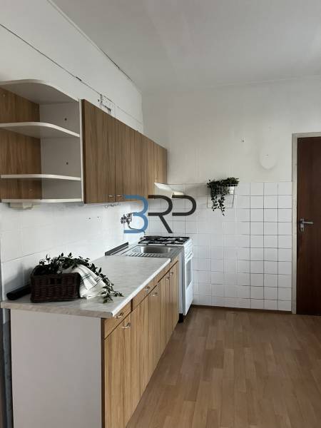 A kitchen in a 2-room apartment with a wood-patterned floor, white tiles, and cabinets.