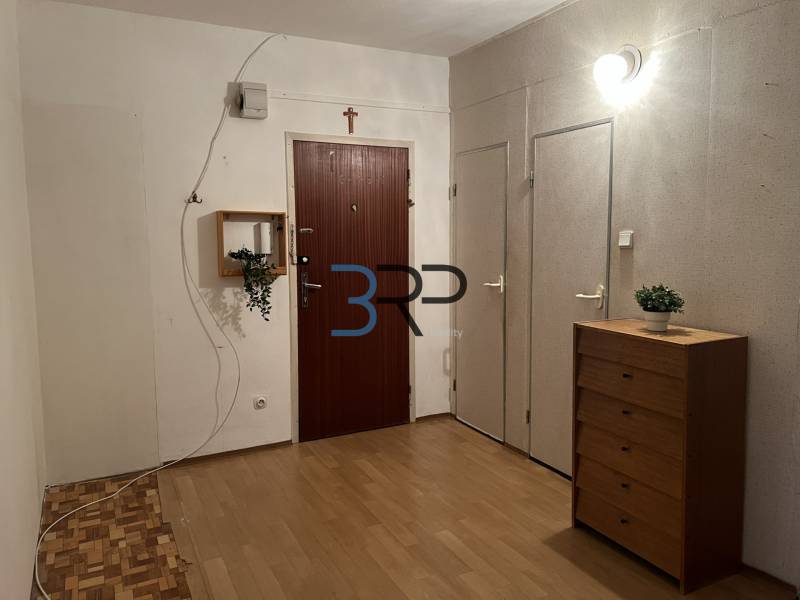 The hallway of a 2-room apartment with a wooden decor floor and a wooden chest of drawers.