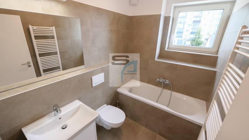 A bathroom in a 2-room apartment with a bathtub, a sink, a mirror, and a window.