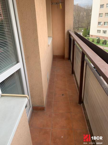 Balcony of a 2-room apartment with terracotta tiles and a view of greenery.