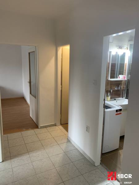 A hallway in a 2-room apartment with a view of the bathroom and a room with a wooden decor floor.