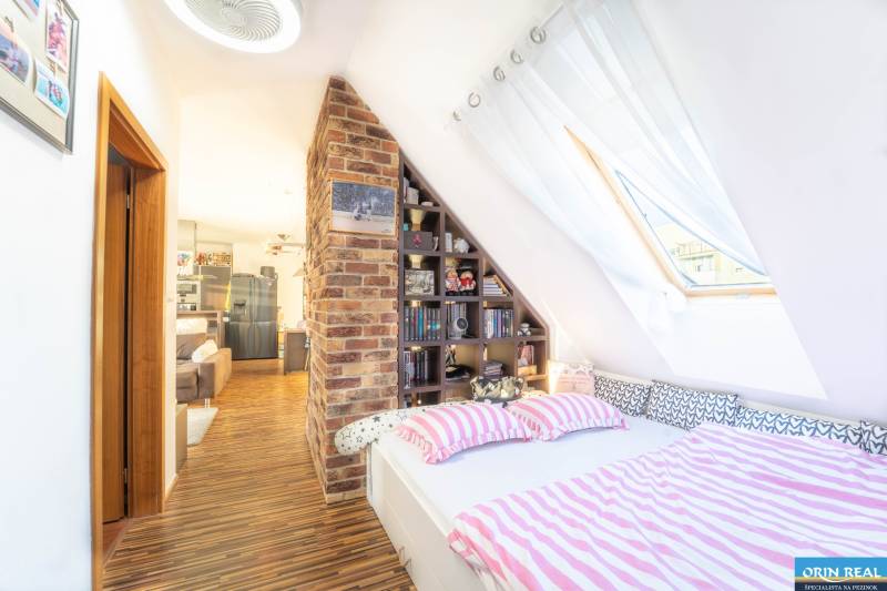 Attic bedroom in a 2-room apartment with brick decor and wood-patterned flooring.