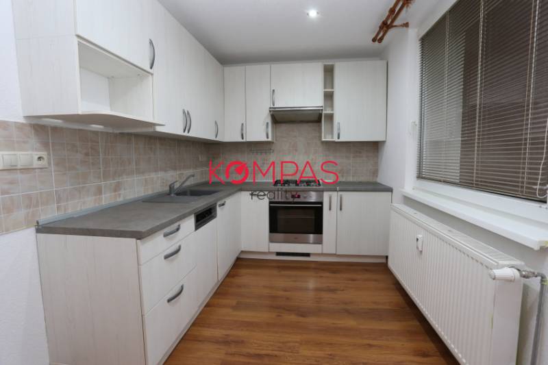 A kitchen in a 3-room apartment with white cabinets and a wood-patterned floor.