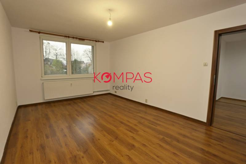 A room with a wooden decor floor in a 3-room apartment, white walls, window, radiator.