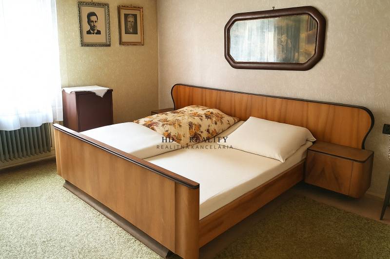 A bedroom with a wooden bed, photographs on the wall, and a mirror in a family house.