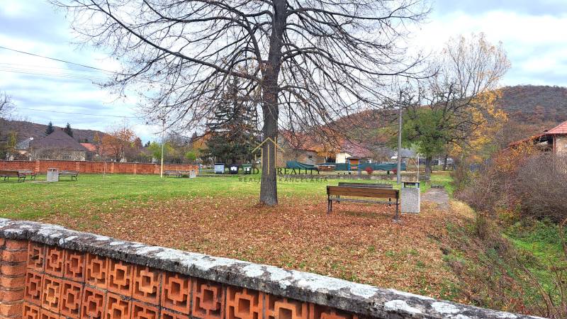 Park in Rykynčice with benches, trees, and a brick fence near a family house.