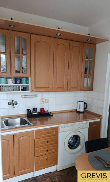 A kitchen unit with cabinets and appliances in a studio apartment, floor with wood decor.