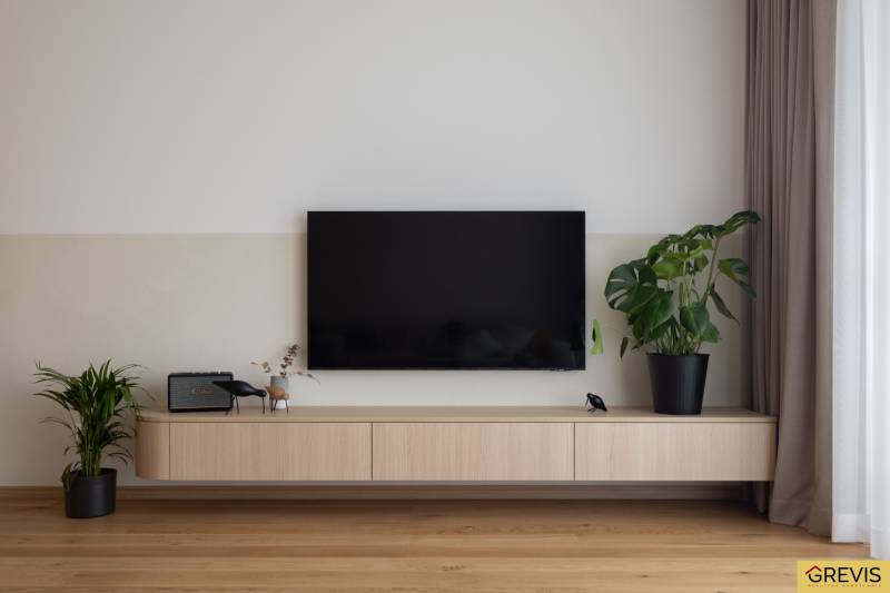 In the 3-room apartment, a television is mounted on a wall with a wooden decor and houseplants.
