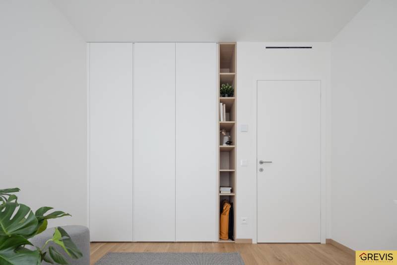 White built-in wardrobe with open shelves in a 3-room apartment with a wooden decor floor.