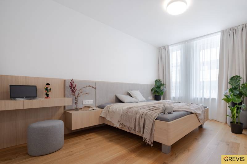 A bright bedroom in a three-room apartment with a wooden decor floor, plants by the window.