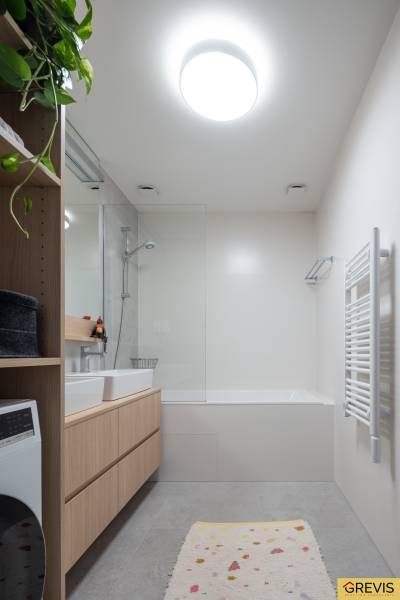 A bathroom in a 3-room apartment with a bathtub, sink, shelf, and washing machine.