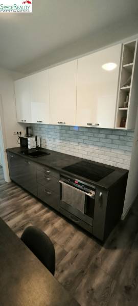 A kitchen in a 3-room apartment with dark cabinets and a wooden-patterned floor.