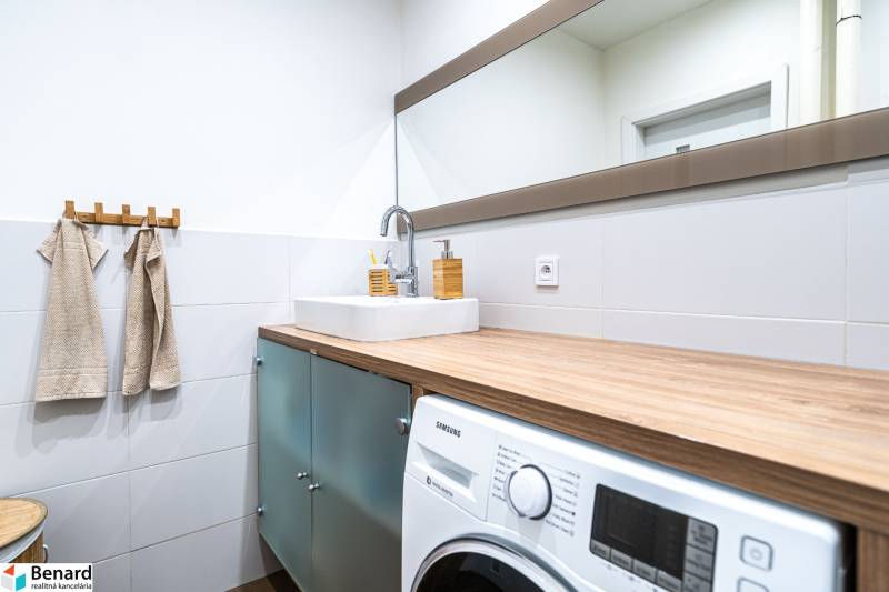 Bathroom with a washing machine, large mirror, and sink in a 3-room apartment with wooden decor.