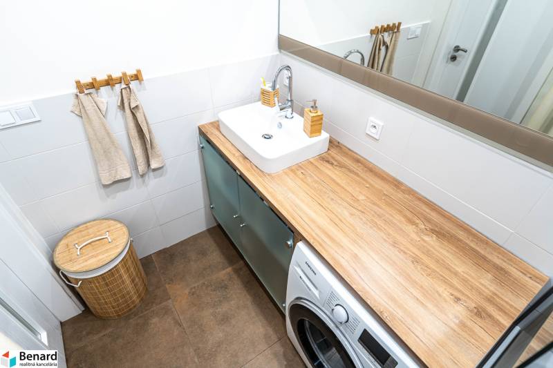 A bathroom with a sink, washing machine, and a floor with a wooden decor in a 3-room apartment.