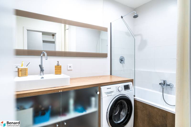 Bathroom with a sink, washing machine, and bathtub in a 3-room apartment, floor with wood decor.