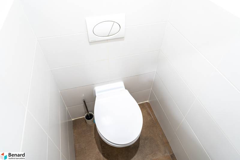 A toilet in a 3-room apartment with white tiles and a dark floor.
