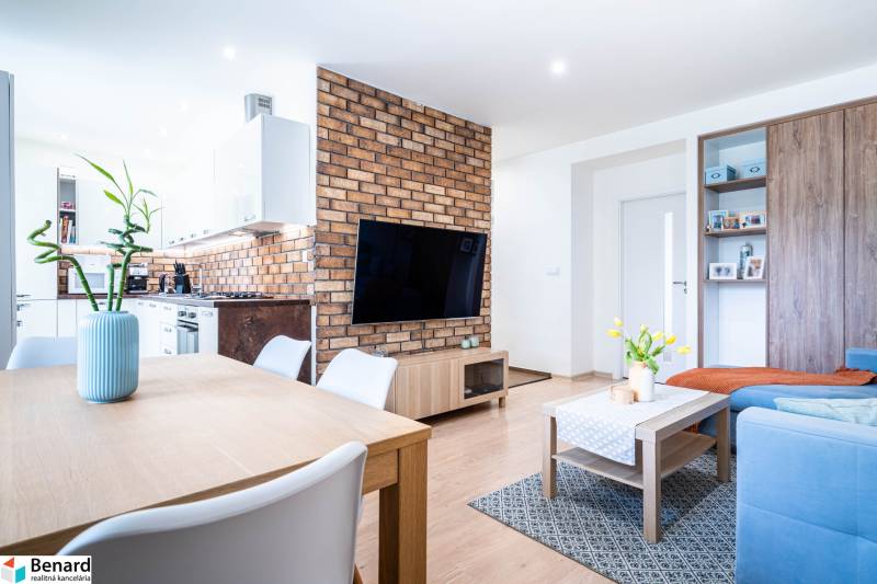 Living room with brick cladding, wood-patterned flooring, and a kitchen in a three-room apartment.
