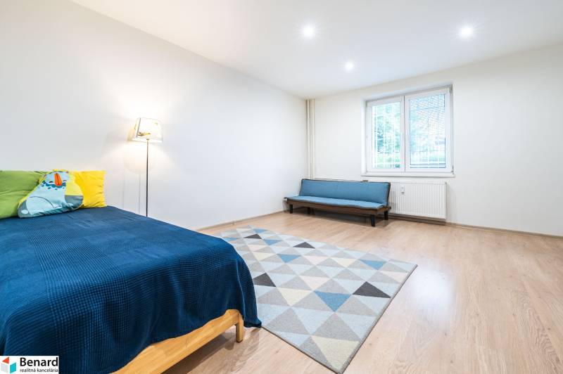Bedroom in a 3-room apartment, blue bedspread, sofa, carpet, wooden decor flooring.